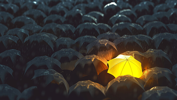 Image of a sea of black umbrellas with a glowing yellow umbrella in their midst